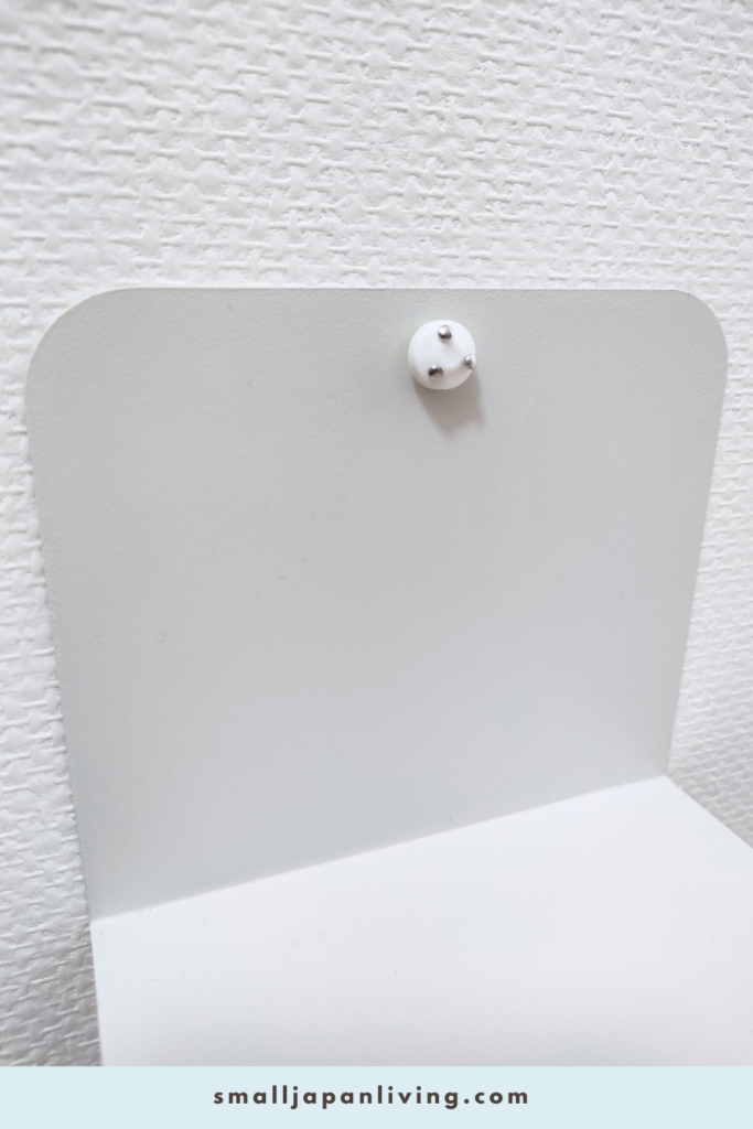 Close-up of a bookend secured to a wall using removable wall pins, creating a stable no-drill shelf for a small apartment phone charging station